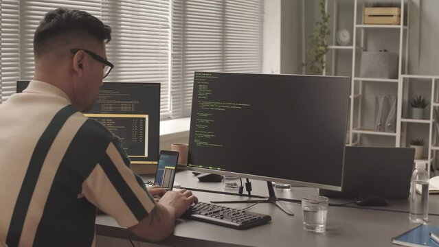 Slowmo of Asian male software developer writing program code on computer working in modern office