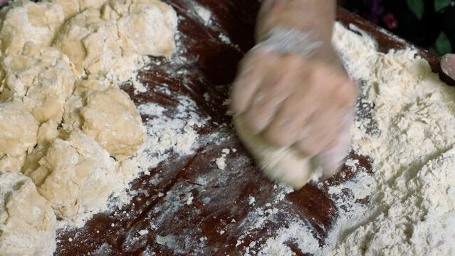 Wrinkled hands of an elderly man knead the dough and make balls of kolobok.
