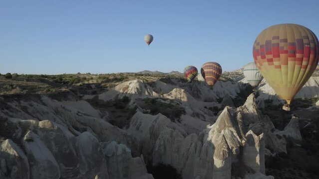 Colorful hot air balloons flying above Love Valley in Cappadocia in Turkey during sunrise on a clear bright morning with sunlight and blue sky above the famous UNESCO world heritage landscape 