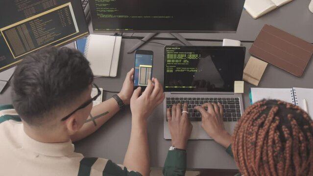 Top view slowmo of two young diverse programmers working with programming code at workplace
