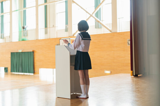 体育館 ステージでスピーチをする女子高生