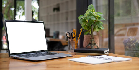 Laptop computer with white screen, stationery and potted plant on wooden office desk.