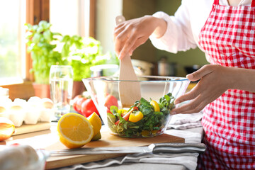Obraz na płótnie Canvas Woman preparing salad at countertop in kitchen, closeup