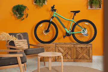 Modern bicycle near orange wall and comfortable armchairs in stylish living room interior