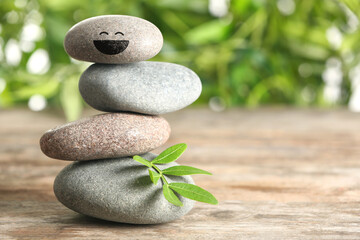 Stack of stones with drawn happy face on wooden table, space for text. Be in harmony and enjoying your life