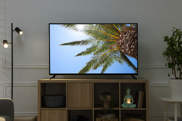 Modern TV set on wooden stand in room. Scene of nature themed movie on screen