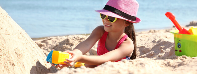 Cute little child playing with plastic toys at sandy beach on sunny day. Banner design