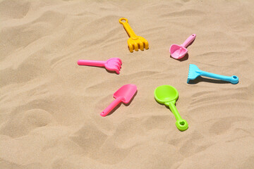 Fototapeta na wymiar Bright plastic rakes and shovels on sand, space for text. Beach toys