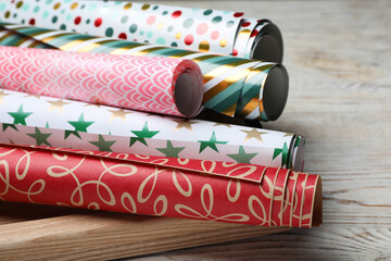 Different colorful wrapping paper rolls on white wooden table, closeup