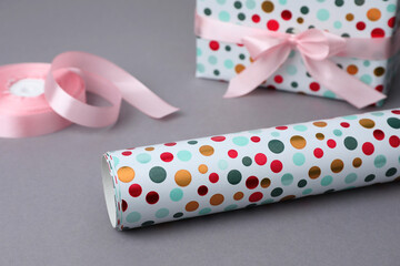 Roll of wrapping paper, gift box and pink ribbon on grey background, closeup