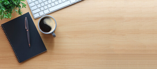 Simple workplace with wireless keyboard, notebook and coffee cup on wooden table. Top view with copy space for your text.