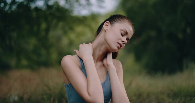 A woman after a sports workout kneads her neck muscles in the park, rest and health care