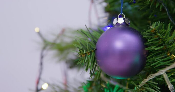 The New Year shiny purpul ball hangs on an artificial Christmas tree against the background of a burning garland. Blurred background. Flickering holiday garland