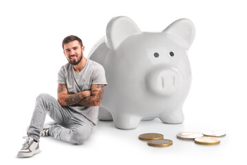 Cool tattooed young man and big piggy bank on white background