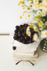 Still life details in home interior of living room. Book, cherries and vase with chamomile flowers. Read and rest. Cozy spring concept.
