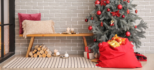 Interior of cozy room with Christmas tree, bench and Santa bag with gifts near grey brick wall