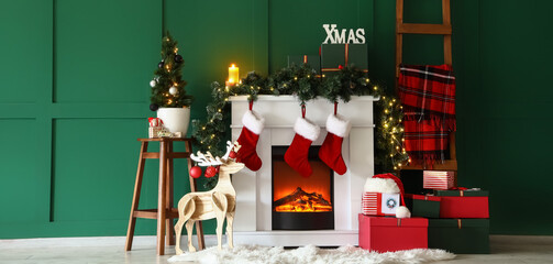 Electric fireplace with Christmas decorations and gifts near green wall