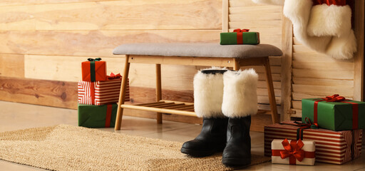 Santa Claus shoes and bench with Christmas gifts near wooden wall in room