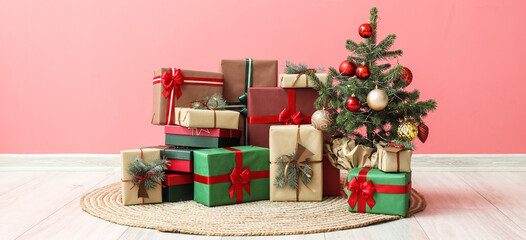 Heap of Christmas gift boxes with fir tree near pink wall in room