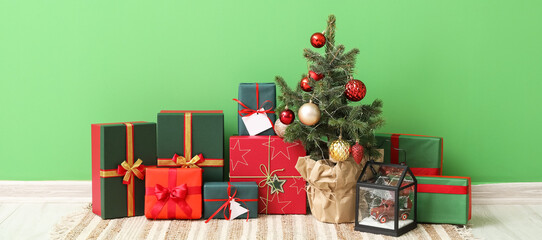 Heap of Christmas gift boxes with fir tree near green wall in room