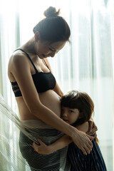 Asian young daughter hug and stroking beautiful pregnant mother tummy.