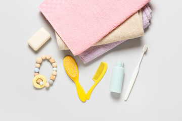Stack of soft towels and different bath accessories for baby on light background