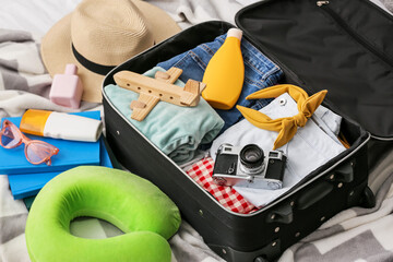 Opened suitcase with clothes, wooden plane and accessories for travelling on plaid