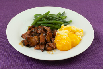 Warm freshly cooked dinner of beef brisket with barbecue sauce and seasoned green beans and grits with cheese on plate