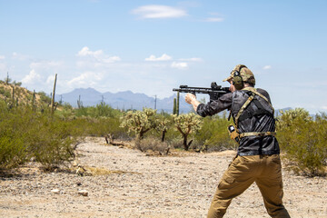 Military special forces person shooting ar15 pistol gun while wearing ear protection and looking through holosight of custom weapon