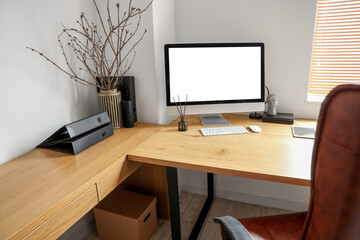 Modern workplace with computer, tablet and tree branches in vase near light wall