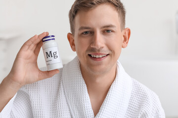Young man with bottle of magnesium pills in bathroom, closeup