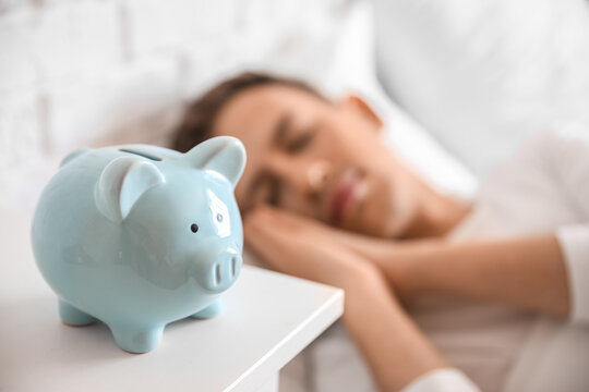 Piggy bank on table of sleeping young man in bedroom, closeup
