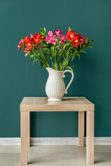 Vase with bouquet of beautiful alstroemeria flowers on table near color wall