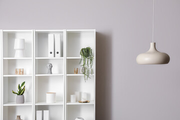Big shelving unit with decor and hanging lamp near light wall