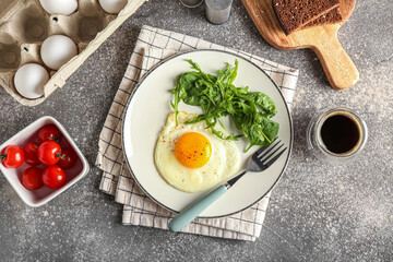 Plate with tasty fried egg, greens, tomatoes and cup of coffee on grunge background