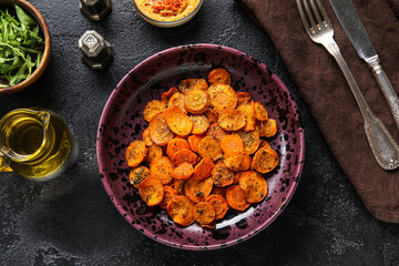Bowl of tasty baked carrots on dark background