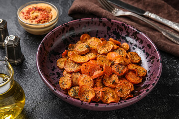 Bowl of tasty baked carrots on dark background, closeup