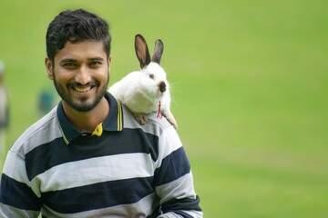 A handsome Indian Asian man, boy, male along with rabbit on shoulder showing animal, pet love....