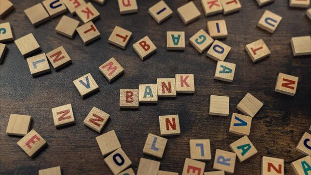 BANK. Money and savings concept. Scattered colourful wooden letter puzzles creating the word bank. Wooden table as a background. Top view. High quality 4k footage