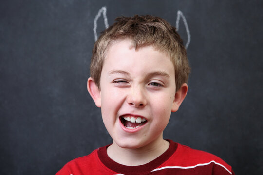 Boy in front of blackboard with devil horns drawn in chalk