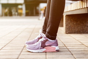 woman in black jeans and sneakers sits on bench. Womens legs in pink sneakers close up