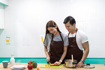 Young asian family couple having fun cooking together and preparing salad with cook food on counter standing on table.Happy couple looking to preparing food the n kitchen