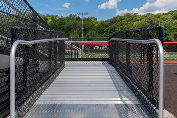 Accessible wheelchair ramp with railings and slip resistant surface at empty metal stadium bleacher.
