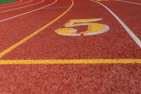 Close up lane number 5 on a new red running track with white lane lines and other markings.	