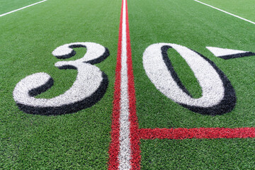 Synthetic turf football 30 yard line in white with black number shadow along with red lacrosse line...