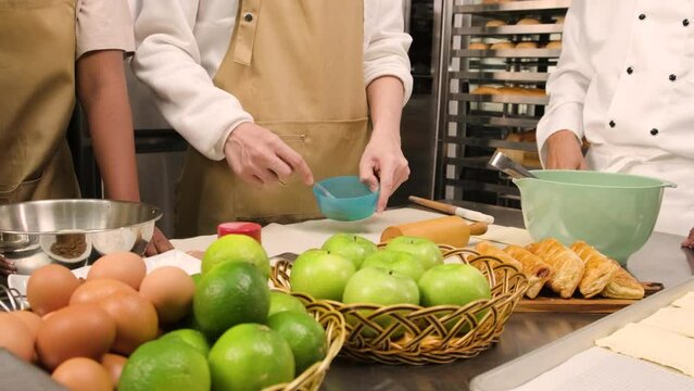 In close-up shots in culinary course class, a uniform chef student with an apron beats eggs and stirs, mixes with pastry dough, and prepares baking bakery food ingredients, fruit pie in the kitchen.