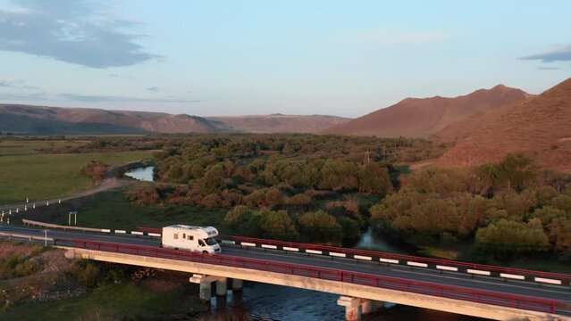 Drone follows camper van rv from the side it sunset on road in wilderness