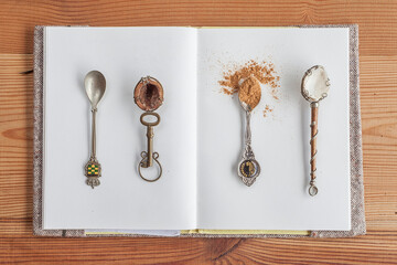 Four handmade teaspoons with ground coffee on a notebook of white leaves