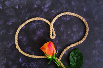 Heart shape made with rope and rose on a dark background. Top view