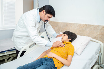 Fototapeta premium Indian doctor of pediatrician holding stethoscope checking heartbeat of sick boy kid at hospital. health checkup, children medical insurance care.